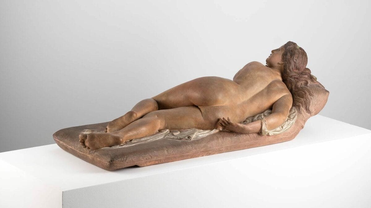 A polychrome terracotta figurine of a nude woman reclining on a couch. This work, named "The Vanity," was created and painted by Joseph Félon for the 1866 Salon.
