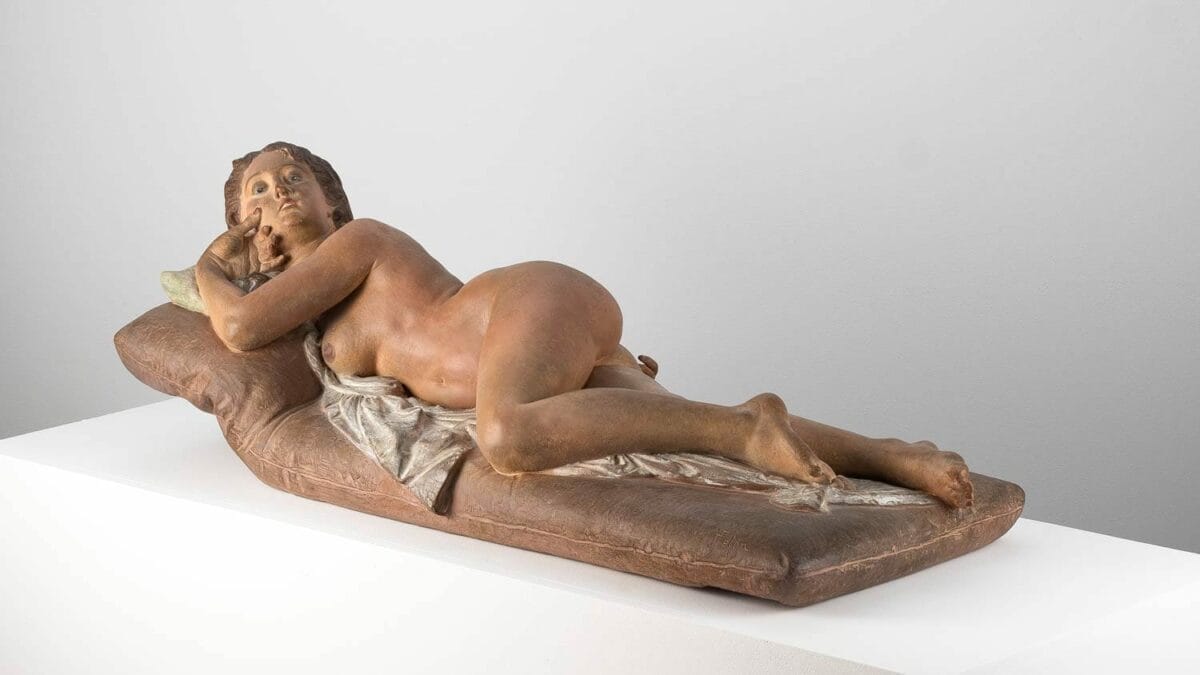 A polychrome terracotta sculpture of a nude woman lying on a divan. Named "The Vanity," it was crafted and painted by Joseph Félon for the 1866 Salon.